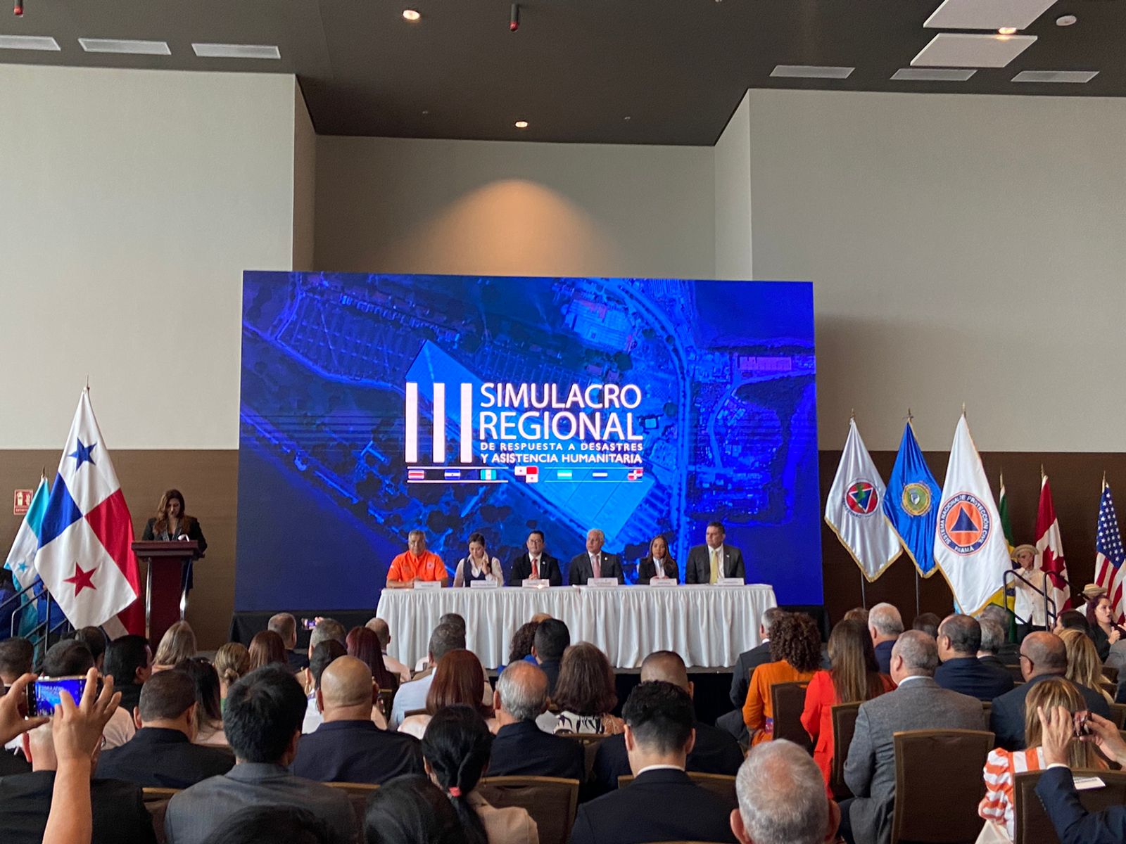 Six panelists sit on stage with a speaker at the podium, opening the 3rd Regional Simulation Exercise for Latin America and the Caribbean in June 2023 in Panama City, Panama.