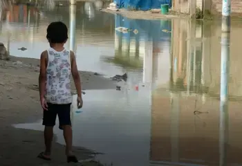 A child walks along the edge of water flooding a street in Piura, Peru