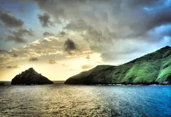 Sunset in the Pacific, showing dark clouds and golden light falling on water and a green island