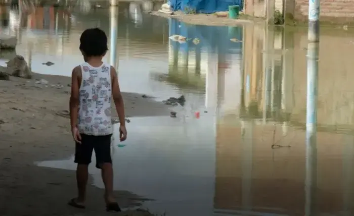 A child walks along the edge of water flooding a street in Piura, Peru