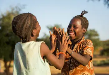 Two girls from Burkina Faso smiling at each other while playing