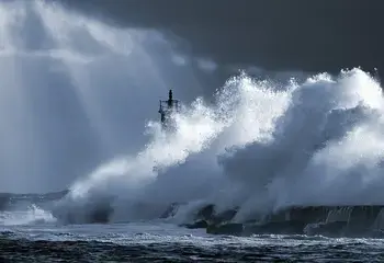A lighthouse stands strong against a huge wave during a storm, guiding ships to safety despite the difficult circumstances. An inspiration to all of us in the context of climate and disaster resilience.