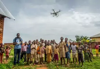 Children and a few adults stand together in a rural community in the Democratic Republic of Congo with a drone flying overhead. Photo: UNDP DRC/Aude Rossignol
