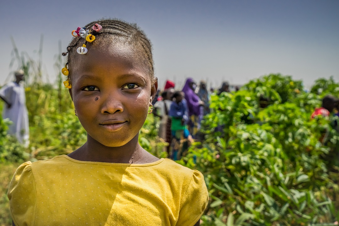 A little girl smiles to the camera in front of a crop field in Mali