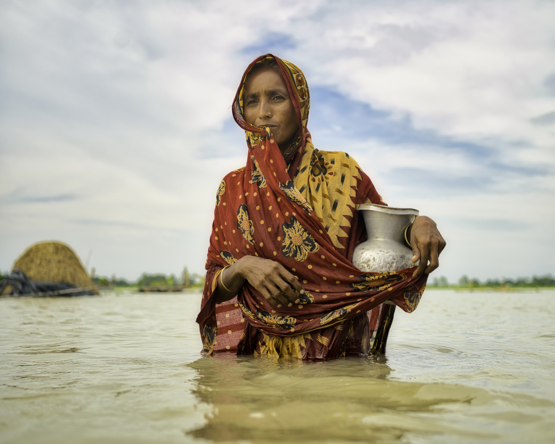 A woman walks in water carrying drinking water, in Bangladesh