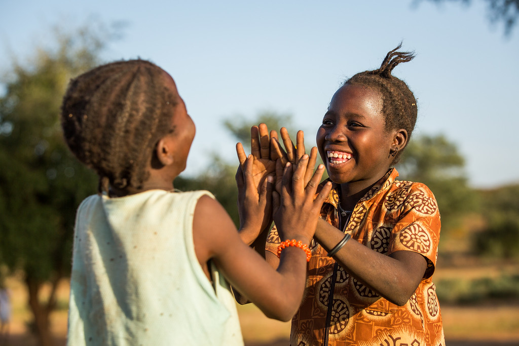 Two girls from Burkina Faso smiling at each other while playing