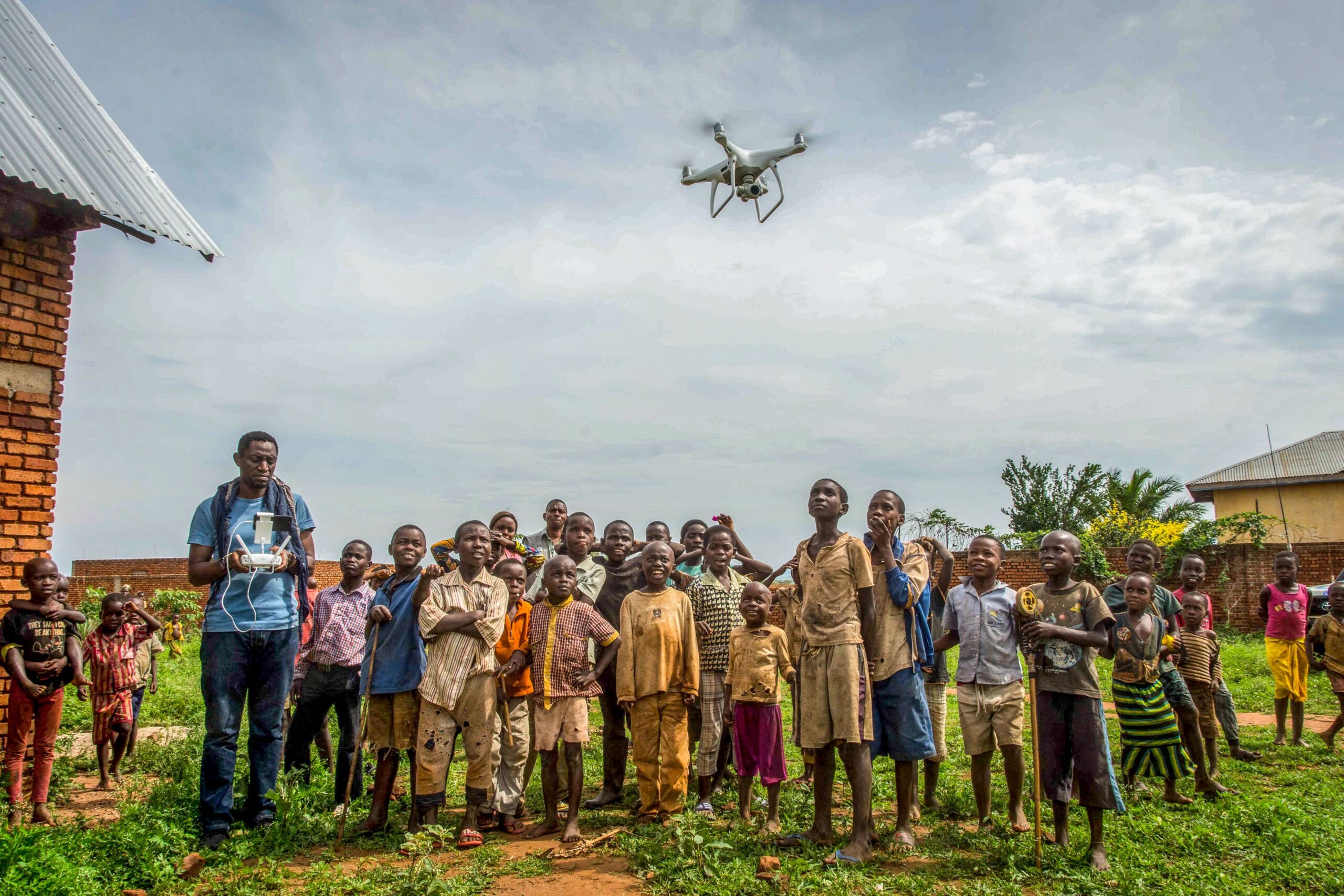 Children and a few adults stand together in a rural community in the Democratic Republic of Congo with a drone flying overhead. Photo: UNDP DRC/Aude Rossignol