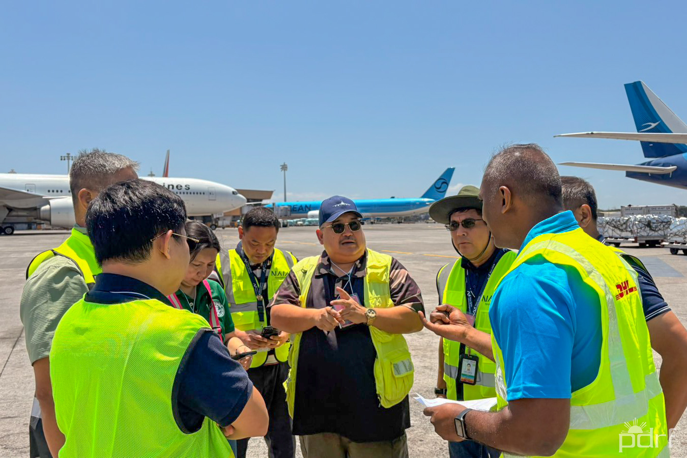 Out on the airfield, with commercial aircraft taxiing in the background, the conversation turns practical: where would extra planes park, and how quickly could relief cargo move from tarmac to truck? Photo credit: PDRF